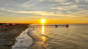 A pier extending into calm waters at sunset with a beach on the left. - Sunny Daze OKI - 4BR Home | 2K, 2Q Beds | Golf Cart | Walk to Beach & Shopping (Oak Island)
