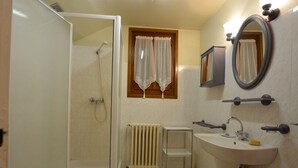 Un bagno con doccia, lavandino, specchio e termosifone.