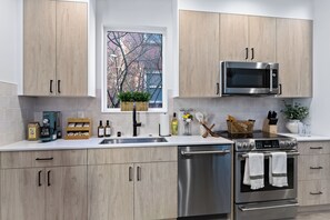 A modern kitchen with wooden cabinets, stainless steel appliances, and a window with a view of trees.