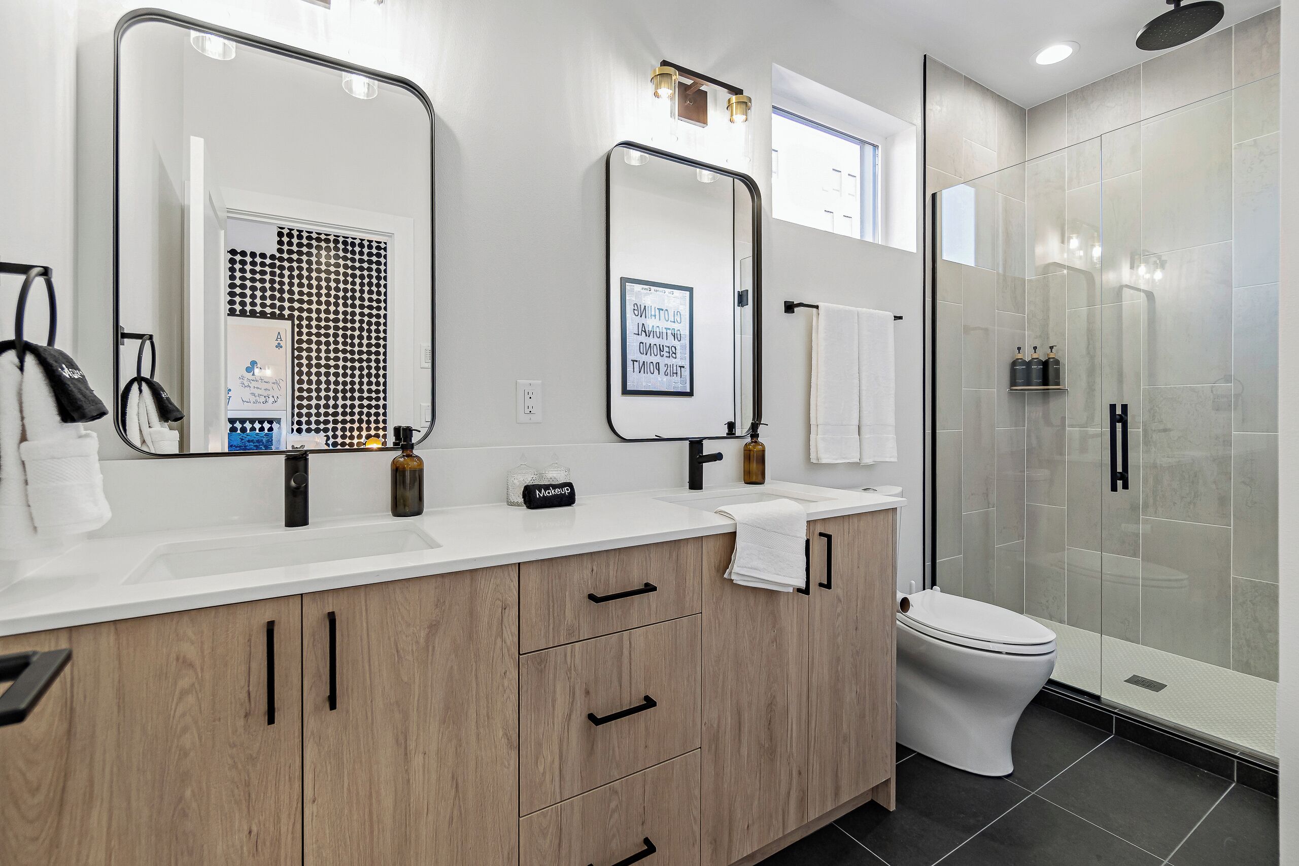 A modern bathroom with a large mirror, a vanity with a sink, a toilet, and a glass-enclosed shower.