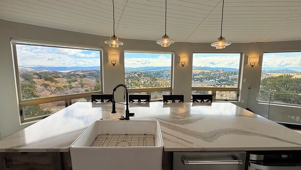 A kitchen with a large island, a built-in sink, and a dishwasher. There are three pendant lights above the island. - Working Ranch House with Astonishing Mountain & Valley Panoramic Views (Cañon City)
