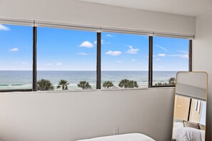 A hotel room with a large window offering a view of the ocean and palm trees. - Luxury Oceanfront 2BR | Includes 4 Beach Chairs (Panama City)