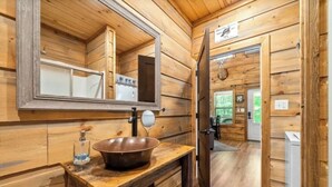 Baño de cabaña de madera con un espejo grande, un lavamanos de madera y una estufa de acero inoxidable.