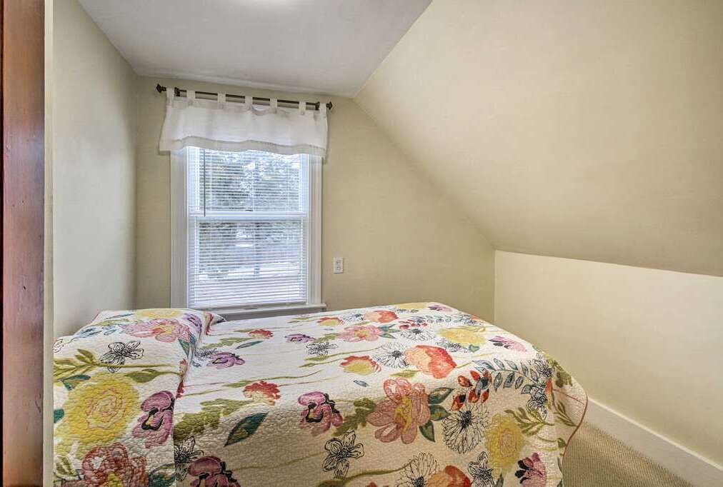 Ein Schlafzimmer mit einem blumigen Bettüberwurf, einem Fenster mit Jalousien und einer schrägen Decke.