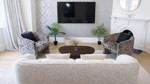 A living room with a large flat-screen TV mounted on the wall, two leopard print armchairs, a white sofa, and a coffee table. There are two potted plants and a fireplace with a white mantel. - Haven Hobart CBD (Hobart)