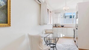 A modern kitchen with white cabinets, a dining table with chairs, and a view of buildings outside. - Haven Hobart CBD (Hobart)