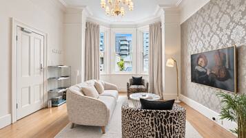 A modern living room with a sofa, a patterned coffee table, a leopard print rug, a painting, and a potted plant.