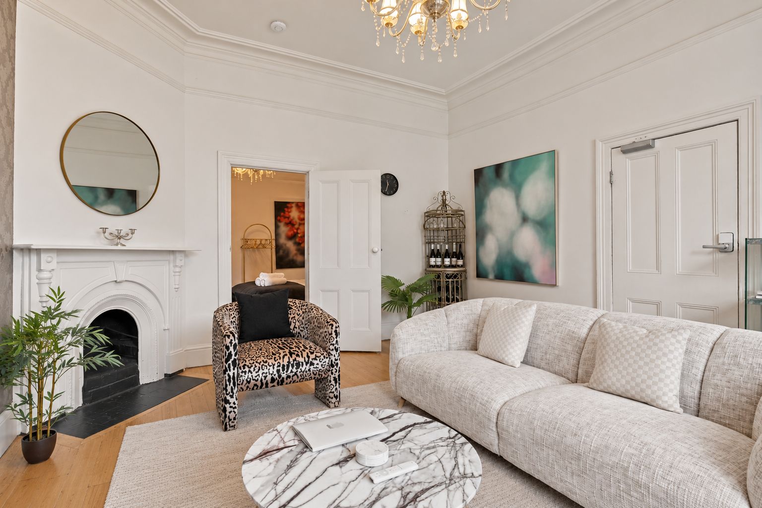 A living room with a fireplace, a sofa, a leopard print armchair, a round coffee table, and a chandelier.