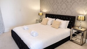 A neatly made bed with white linens and two rolled towels, a dark headboard, and two bedside tables with lamps. - Haven Hobart CBD (Hobart)