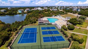Vue aérienne d’un complexe de courts de tennis comprenant plusieurs terrains, une piscine et des maisons résidentielles environnantes.