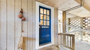 Une façade en bois avec une porte bleue, un porche en bois et une structure en treillis.