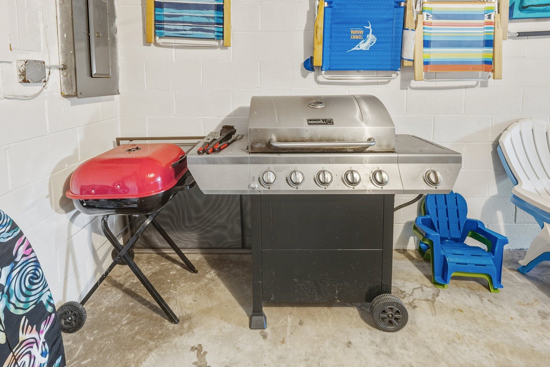 A portable grill with four burners, a red cooler, and a blue folding chair.