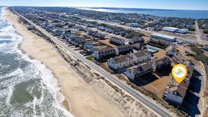 Luchtbeeld van een kustgebied met woningen langs het strand, een weg parallel aan de kustlijn en een groot wateroppervlak in de verte.