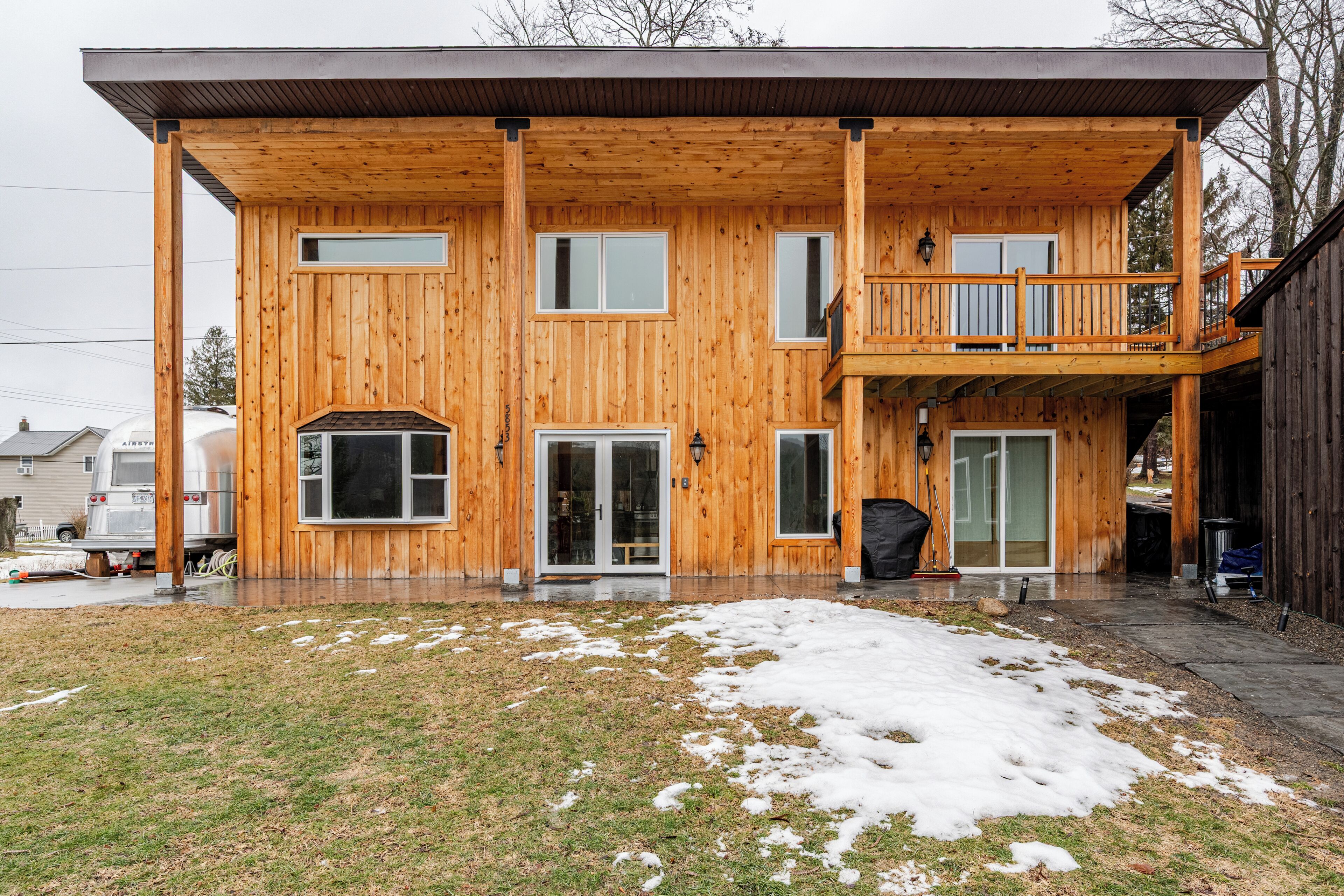 Een houten chalet met twee verdiepingen, een balkon op de bovenverdieping, een voordeur en een garage.