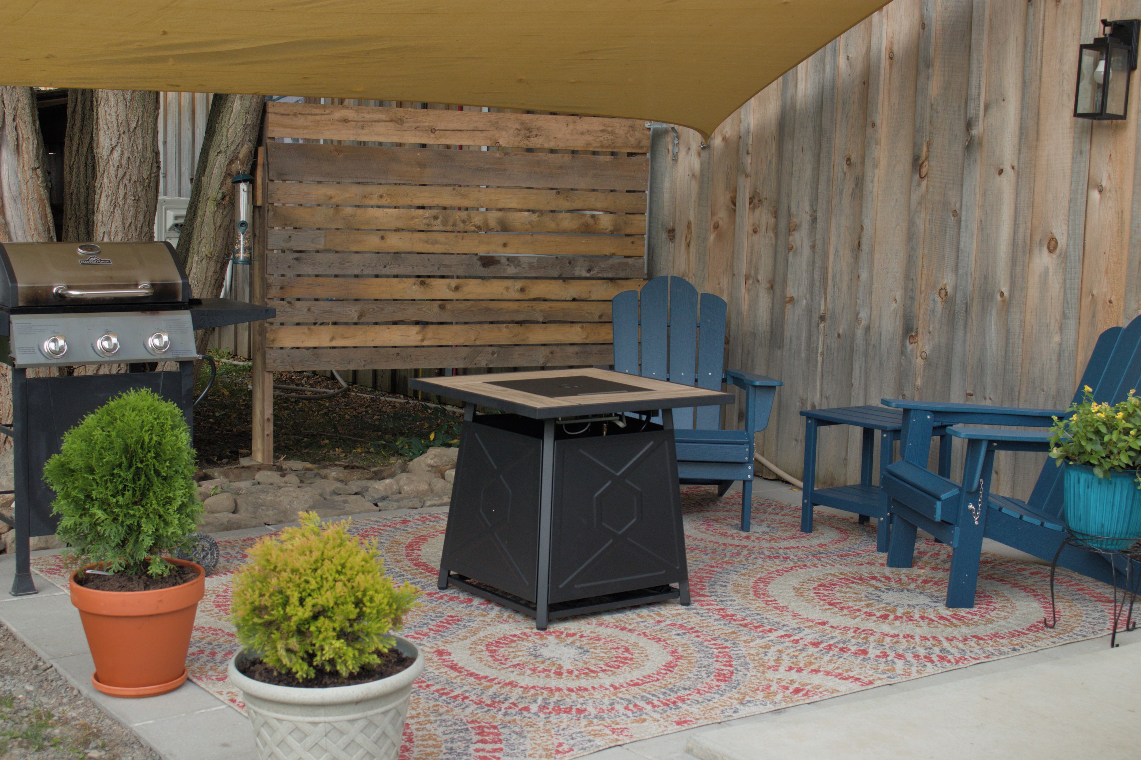 An outdoor patio area with a barbecue grill, two chairs, a small table, and potted plants.