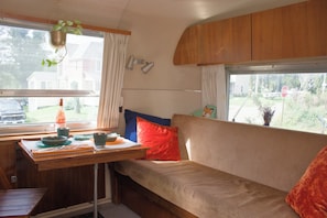 A cozy interior with a sofa, a table with dishes, and a hanging plant. - Vintage Airstream near Watkins Glen (Alpine)