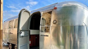 Een klassieke caravan met een geopende deur, die een klein binnenruimte onthult met een trap naar de deur.