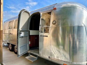 A vintage trailer with a door open, revealing a small interior space with a step leading up to the door.