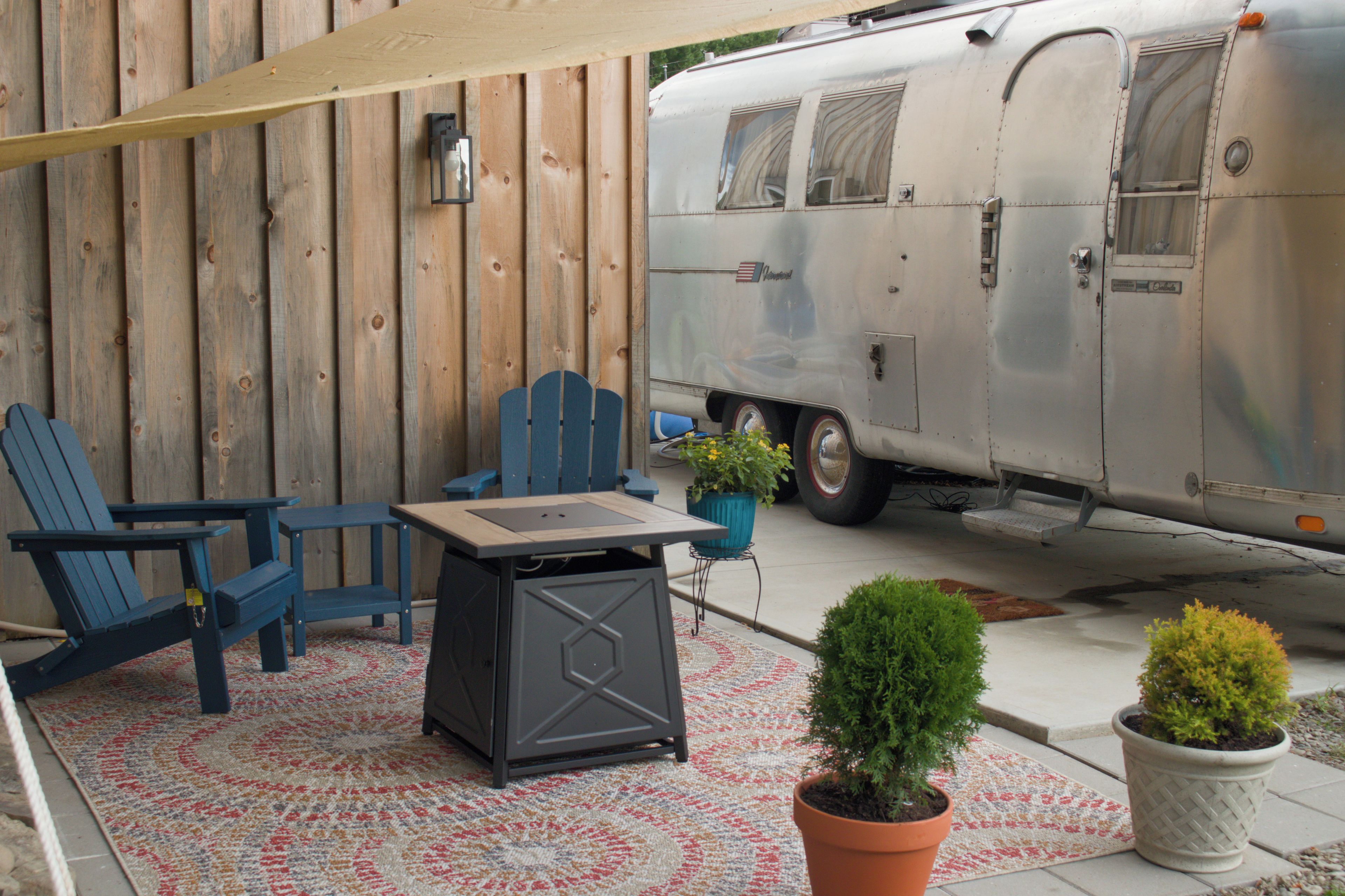 A patio with a table and chairs, a potted plant, and a trailer.
