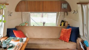 Hyggelig autocamper indretning med sofa, puder, et bord med bestik og et vindue med gardiner.