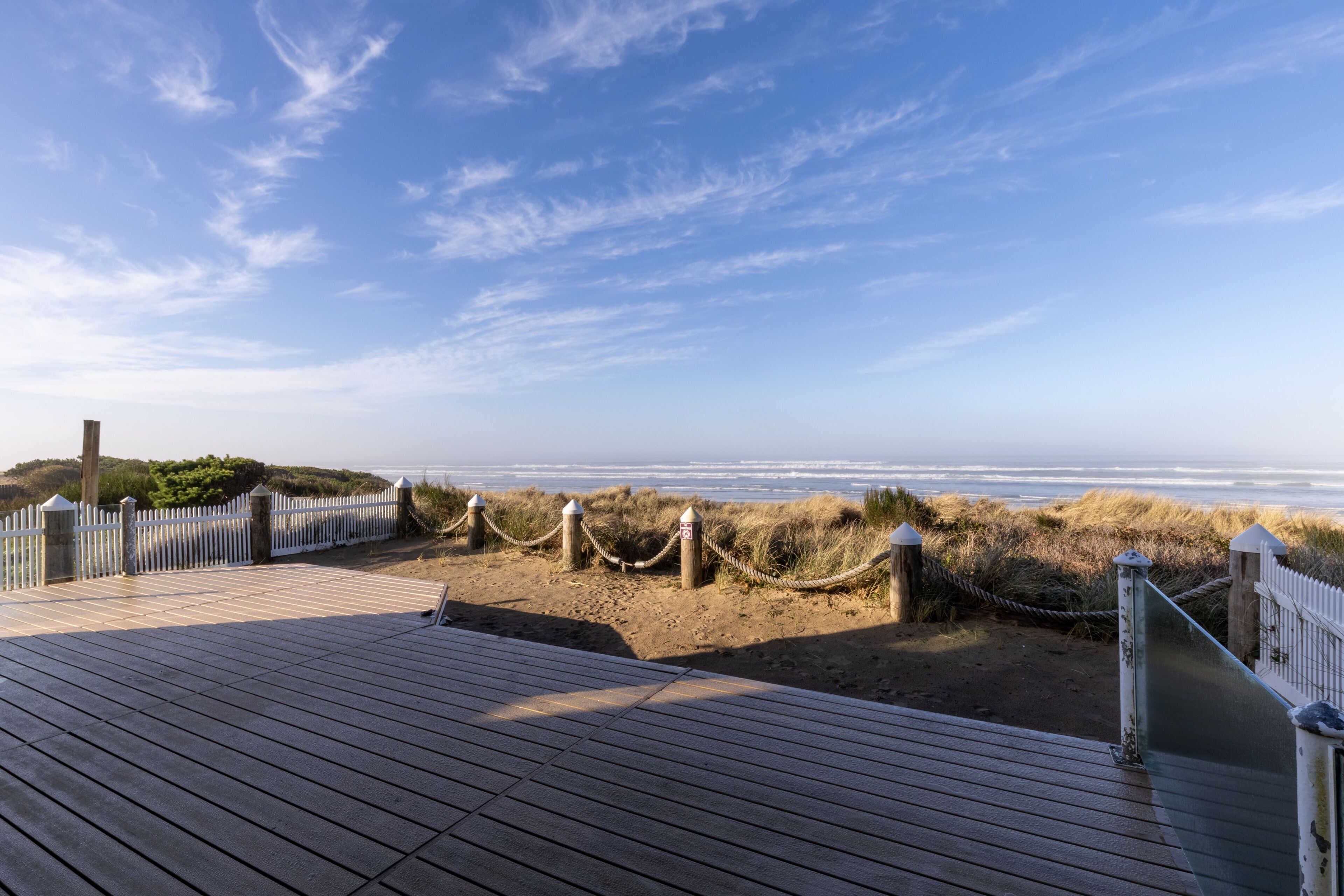 A wooden boardwalk leading to a beach with a white fence and rope barrier.
