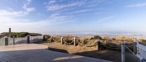A wooden boardwalk leading to a beach with a white fence and rope barrier.