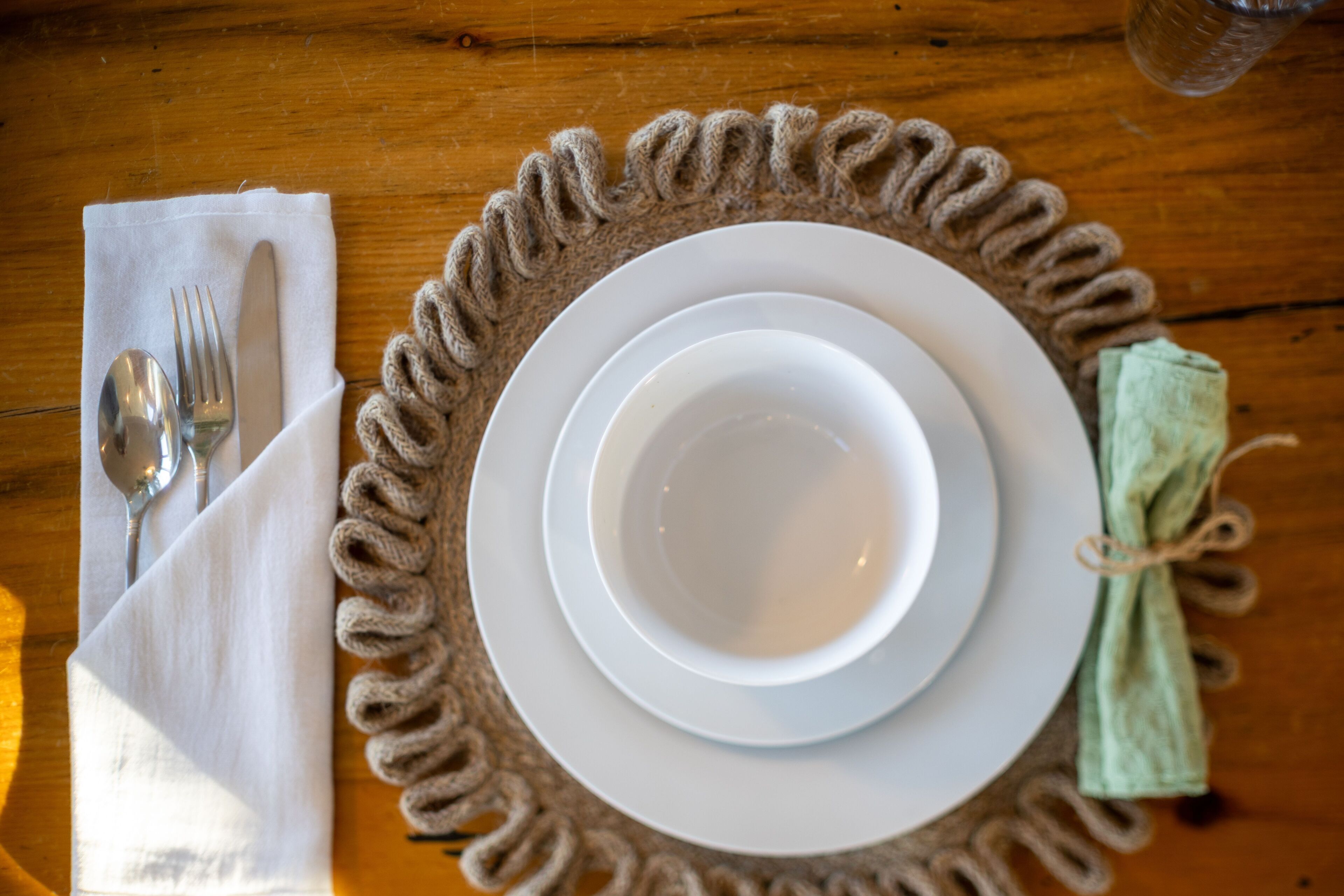 Une table dressée avec de l’assiette blanche, une serviette pliée et des couverts en argent.