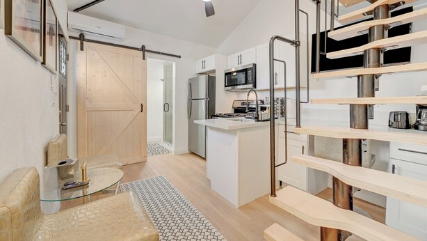 Une cuisine moderne avec des meubles blancs, un îlot central, des appareils en acier inoxydable et un ventilateur de plafond.