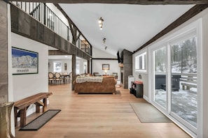 A spacious living area with a wooden floor, a sofa, a fireplace, and large windows with a snowy view.