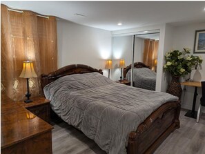 A bedroom with a large bed, wooden headboard, two bedside tables with lamps, a mirror, and a potted plant.