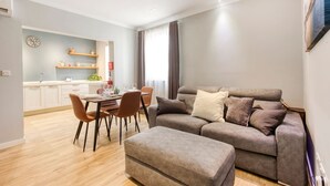 A modern living room with a grey sofa, a dining table with chairs, and a kitchen area in the background. - Central Msida Apartment Workspace Wi-fi A C (Msida)