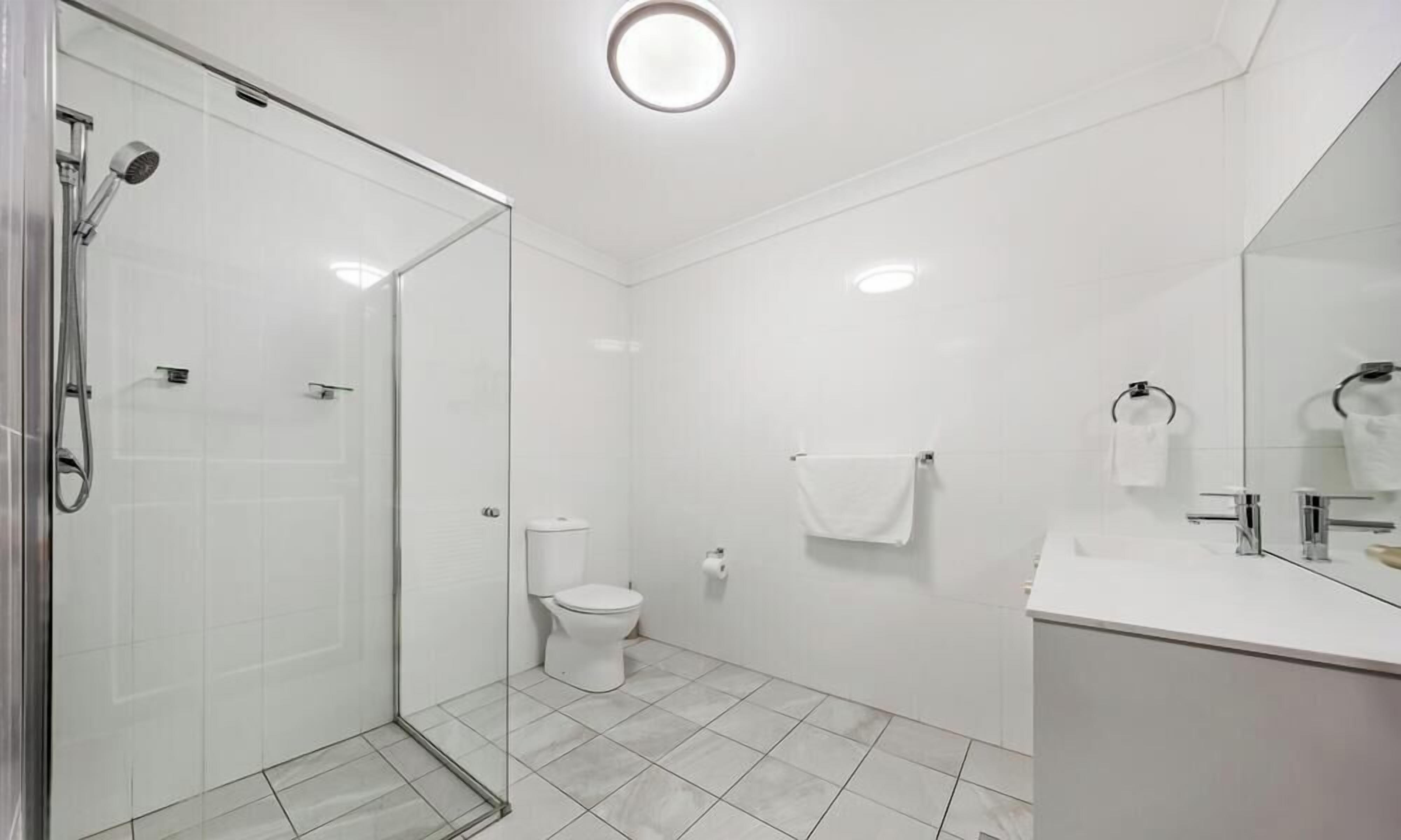 A modern bathroom with a glass shower enclosure, a toilet, and a sink with a mirror.