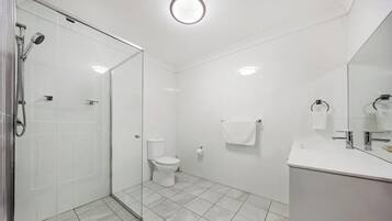 A modern bathroom with a glass shower enclosure, a toilet, and a sink with a mirror.