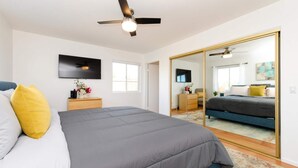 Ein Schlafzimmer mit einem Bett, einem Nachttisch, einem Fernseher, einem Deckenventilator und einem großen Spiegel.