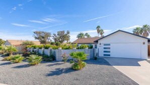 Ein Wohnhaus mit weißer Garage, einem Schotterweg und einem angelegten Garten mit verschiedenen Pflanzen und einem Holzzaun.