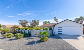 A residential property with a white garage, a gravel driveway, and a landscaped garden with various plants and a wooden fence. - Desert Oasis Pool, Spa & Gorgeous Views to relax (Palm Springs)