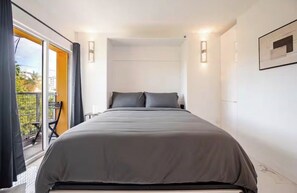 Ein modernes Hotelzimmer mit einem großen Bett, einem Balkon mit Blick und einem schlichten, klaren Design.