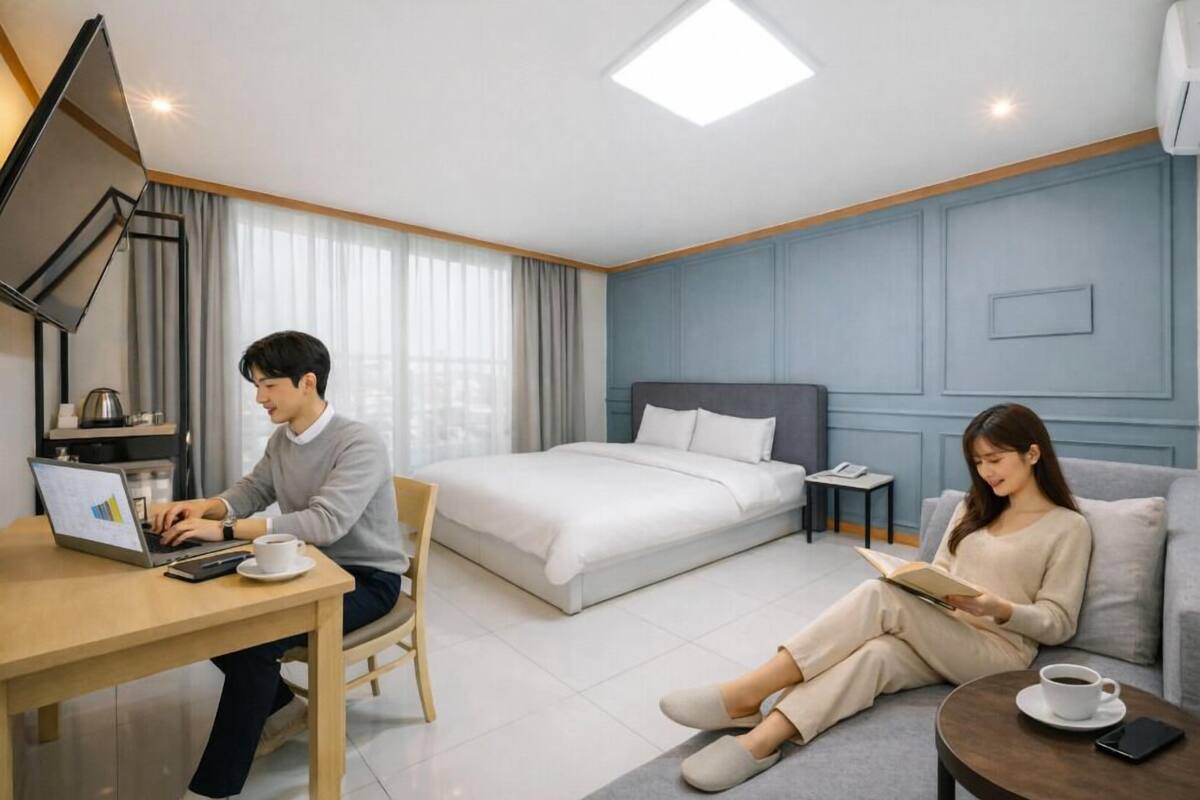 Ein Hotelzimmer mit Bett, Schreibtisch mit Laptop, Stuhl, Sofa, Nachttisch und Couchtisch.