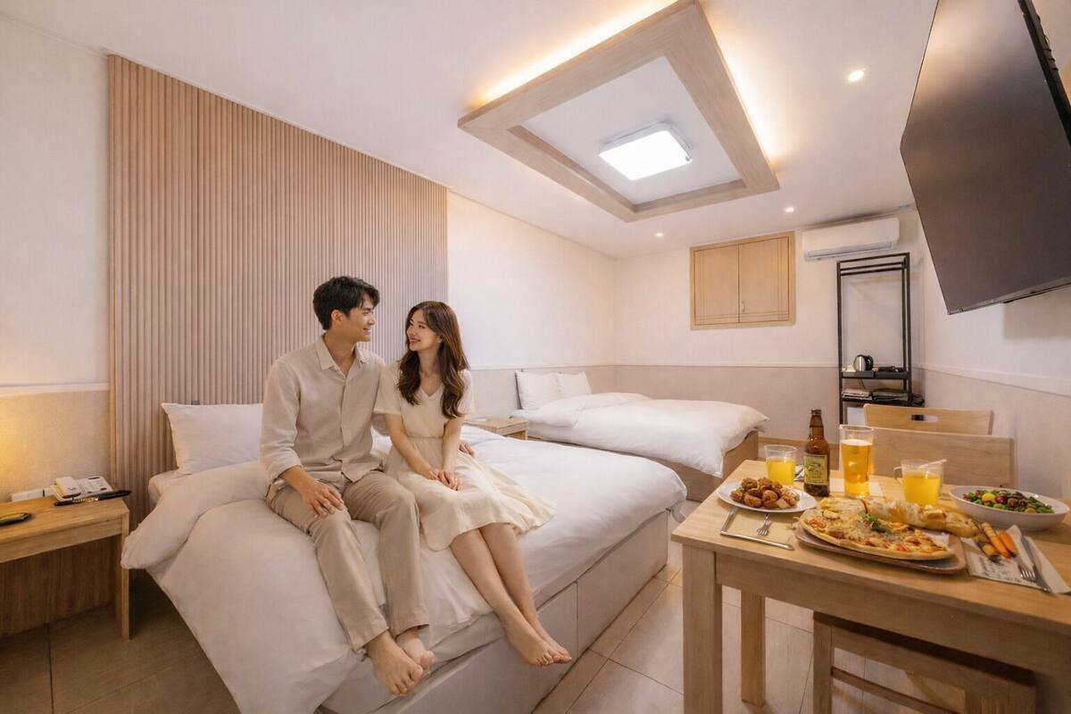 Ein modernes Hotelzimmer mit einem Bett, einem Frühstückstisch mit Speisen und Getränken sowie einem an der Wand montierten Fernseher.
