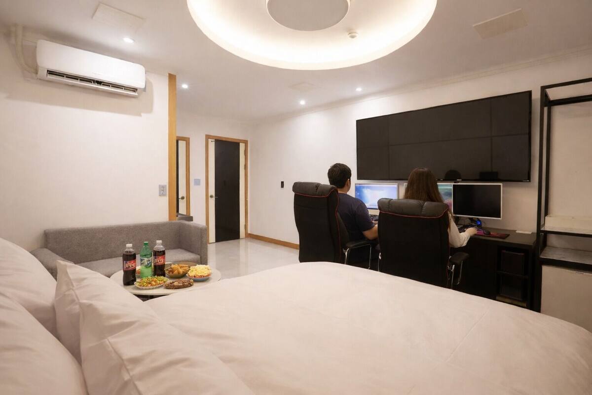Ein modernes Hotelzimmer mit einem Bett, einer Couch, einem Schreibtisch mit zwei Computern und einem Flachbildfernseher.