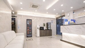 A modern hotel lobby with a reception desk, a white sofa, and a digital screen displaying social media icons. - JM HOTEL (Suwon)