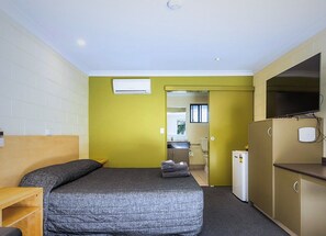 Quarto compacto com cama, pequeno espaço de cozinha e televisão.