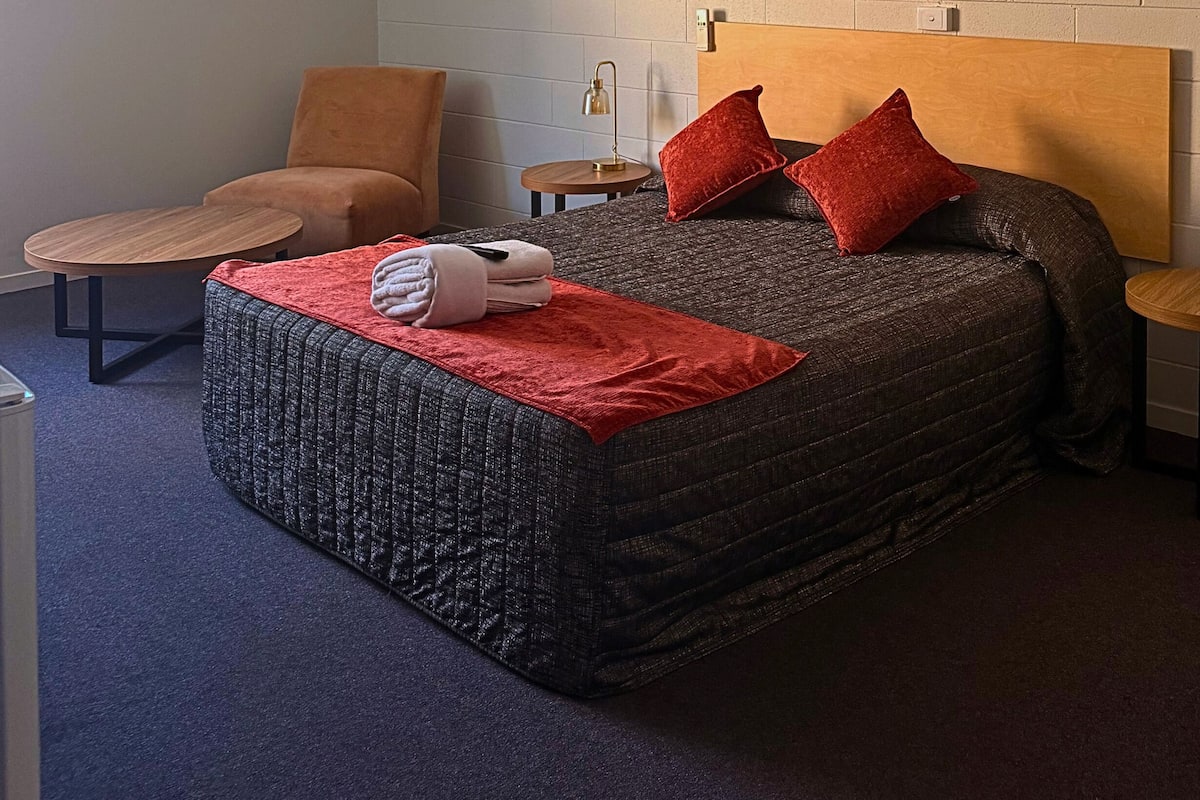 Une chambre à coucher comprenant un lit, une chaise, une petite table et une lampe fixée au mur.