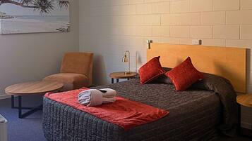 A bedroom with a bed, a chair, a small table, and a wall-mounted lamp.