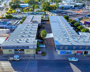 Vista aérea de um edifício comercial com várias vagas de estacionamento, uma rua central e edifícios menores adjacentes.