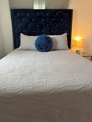A bed with a dark headboard, a decorative blue pillow, and a patterned quilt. - Cozy Stilt Cottage
“Charming Stilt Cottage by Park, Walk to The Brazos River!” (Rosenberg)