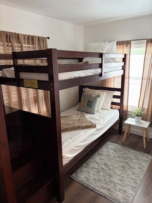 A bunk bed room with a small bedside table and a window with curtains. - Cozy Stilt Cottage
“Charming Stilt Cottage by Park, Walk to The Brazos River!” (Rosenberg)