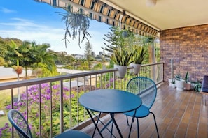 A balcony with a view of a garden and cityscape, featuring a table and chairs. - Beachside Apartment w/ Mountain Views, Near (Burleigh Heads)