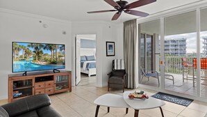 Un salon moderne doté d’un téléviseur à écran plat, d’un ventilateur de plafond, d’un canapé, d’une table basse et d’un balcon aménagé avec du mobilier d’extérieur.