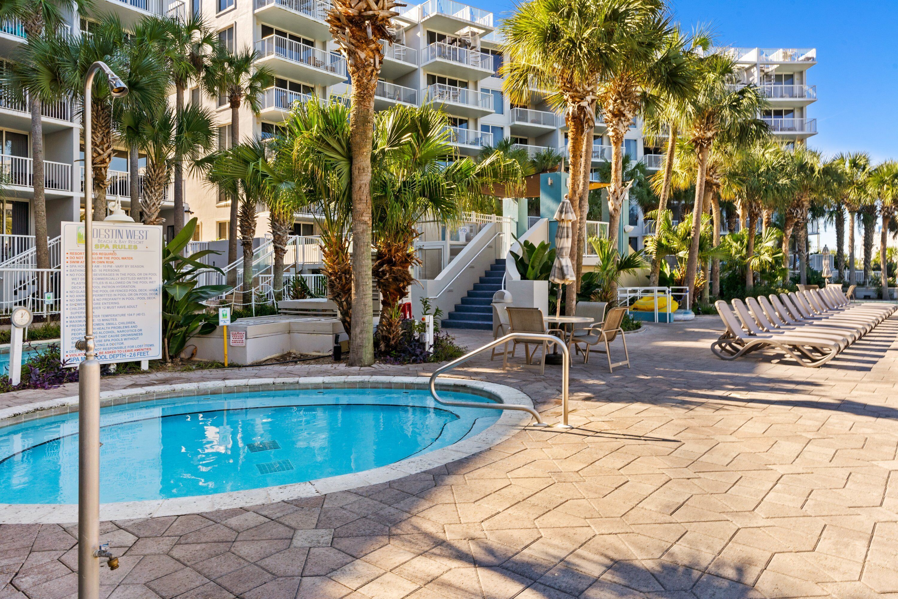 A pool area with lounge chairs, palm trees, and a sign detailing spa rules.